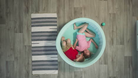 siblings enjoy lying in cyan soft pool near rug on floor