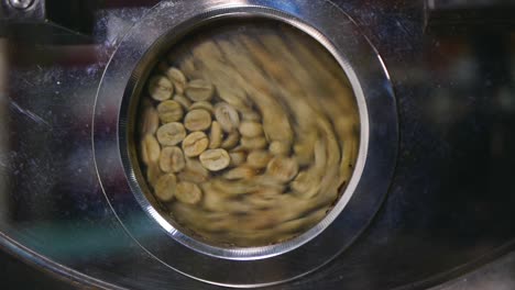cerca de granos de café verde recién secados dando vueltas en la máquina tostadora