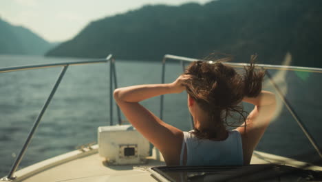 mujer con el cabello desaliñado por el viento mira fuera de la escotilla abierta de la cabina en una lancha a motor navegando en el lago. relajación y vista panorámica en clima cálido