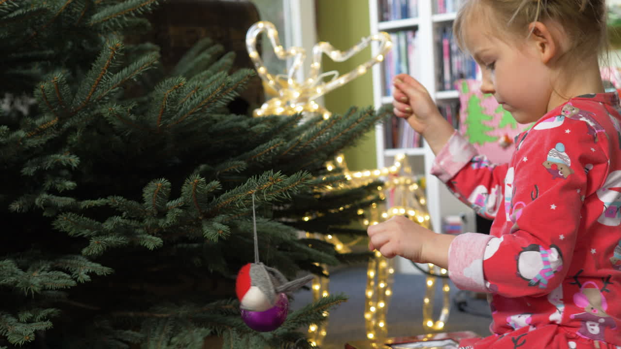 un primer plano de una niña decora un árbol de navidad de pino con adornos