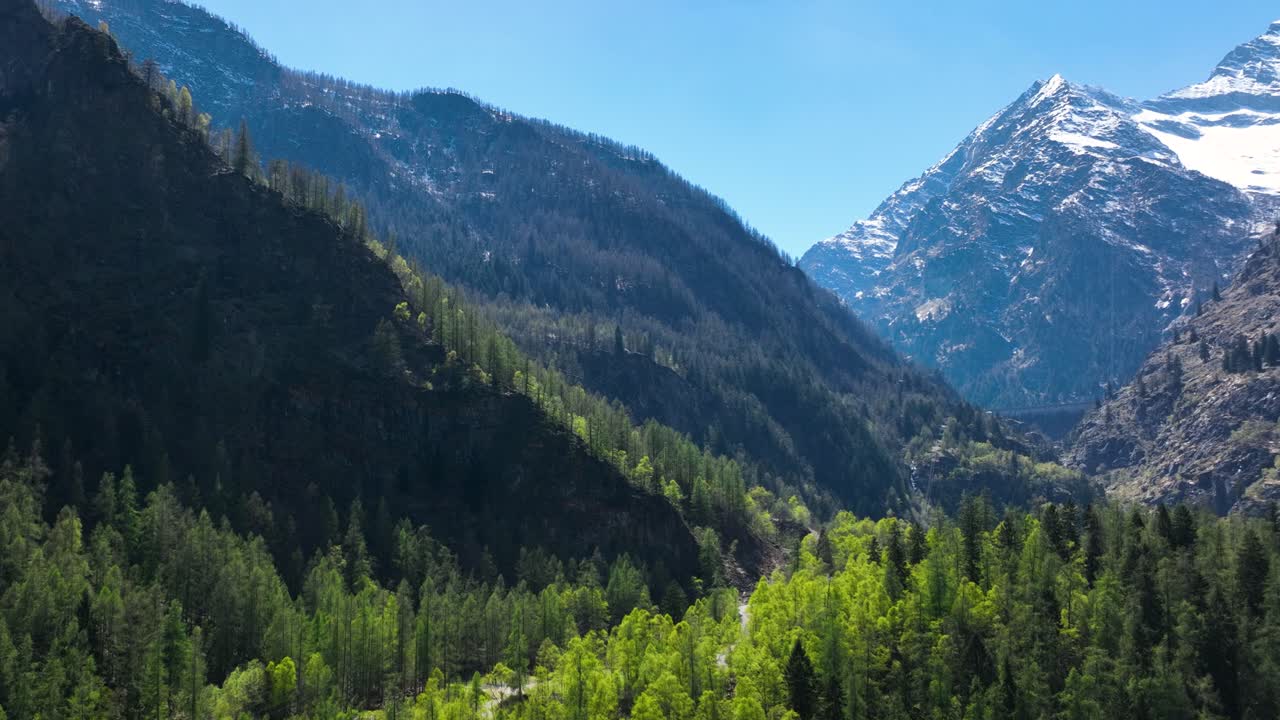 toma aérea desde la derecha de un camión de gran contraste entre montañas cubiertas de bosques verdes y una imponente montaña escarpada cubierta de nieve que se eleva por encima