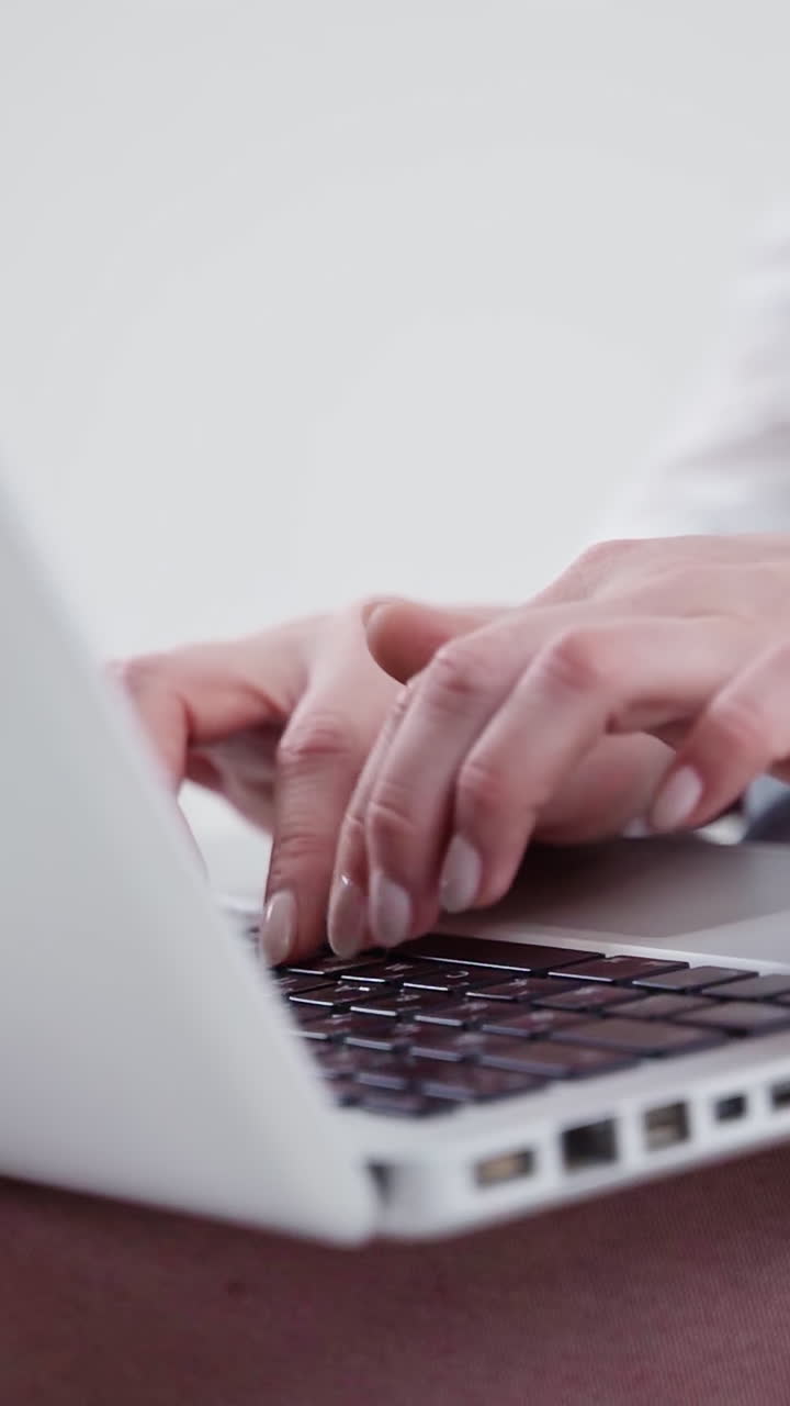 Modern laptop on female's legs. Young woman's hands typing on a white laptop. Close-up. Slow motion. Vertical video