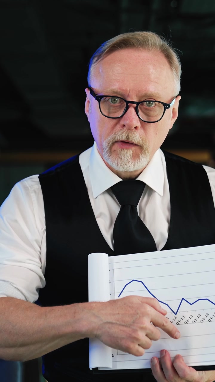 Succesfuld ældre forretningsmand iført briller, hvid skjorte og sort vest viser dokumenterne. Mand forklarer diagrammerne på kontoret. Vertikal video.