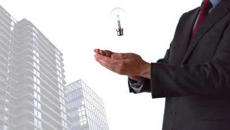 Animation-of-light-bulb-over-businessman-hands-and-modern-buildings-in-background