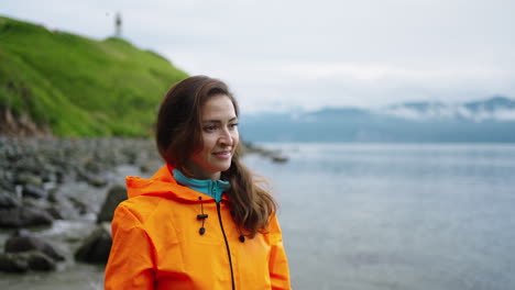 woman in orange rain jacket by the ocean