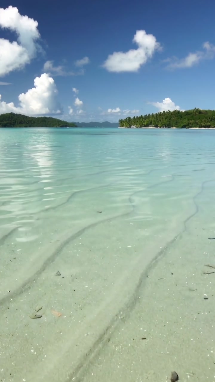 Vertical video: Rippling shallow turquoise water moving over white sand at tropical bay with boat