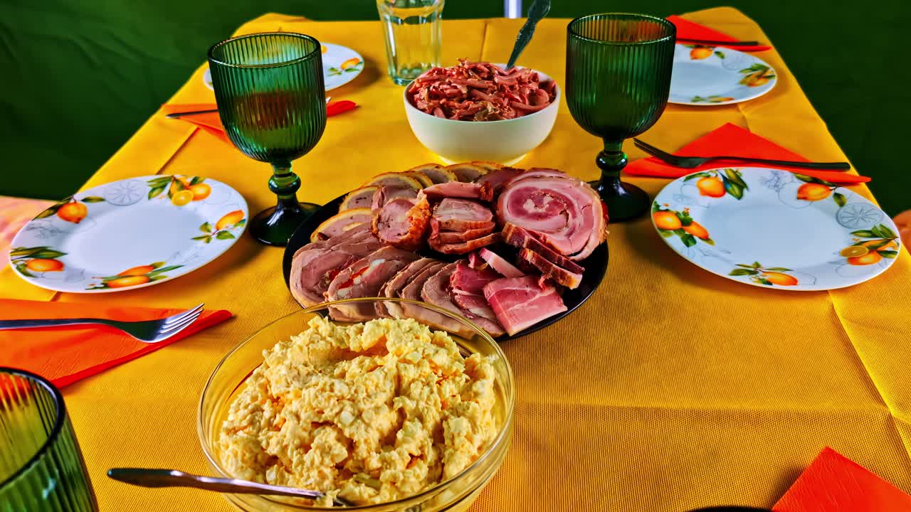 Rustic outdoor table set with sliced meat, salad, and glasses on yellow cloth