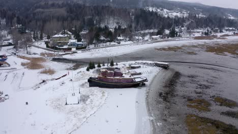 Drone-Volando-Alrededor-De-Un-Hermoso-Barco-Antiguo-Bajo-La-Nieve-En-Un-Astillero-En-Charlevoix,-Quebec