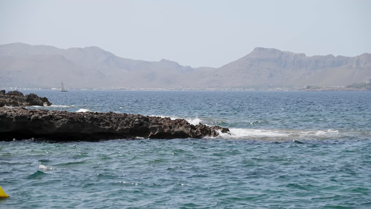 playa rocosa rodeada de montañas con algunos yates al fondo en la isla de mallorca
