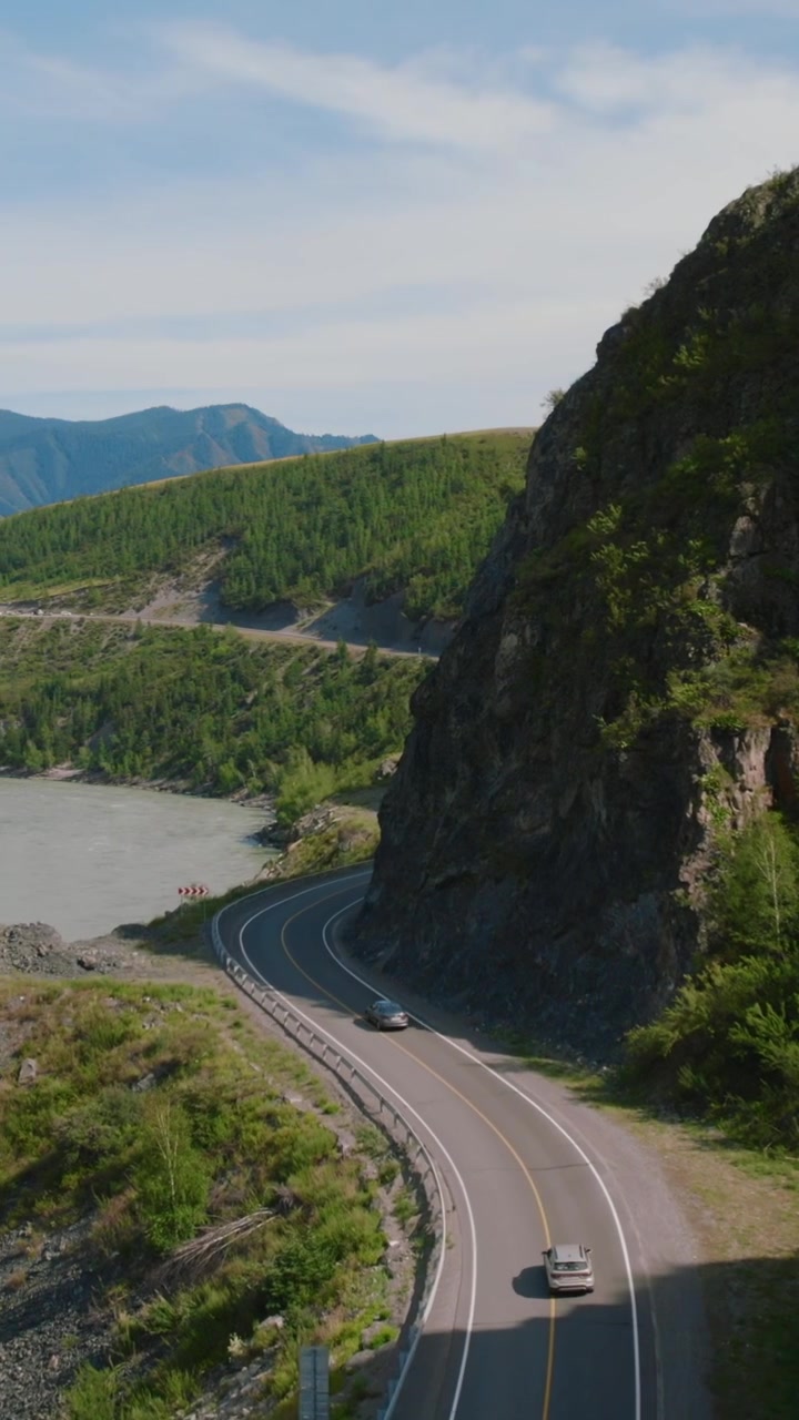 Luftoptagelser af biler, der kører på den snoede Chuysky Trakt-motorvej langs Katun-floden, forbi klippefyldte skrænter og grønne bjerge i Altai, Rusland.