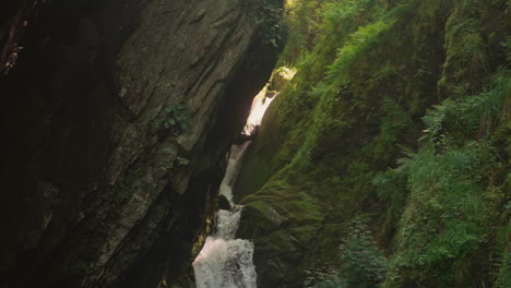 narrow waterfall runs through rocky trench at highland slow motion. cascade stream falls from steep cliff in wild forest. water flow between old stones