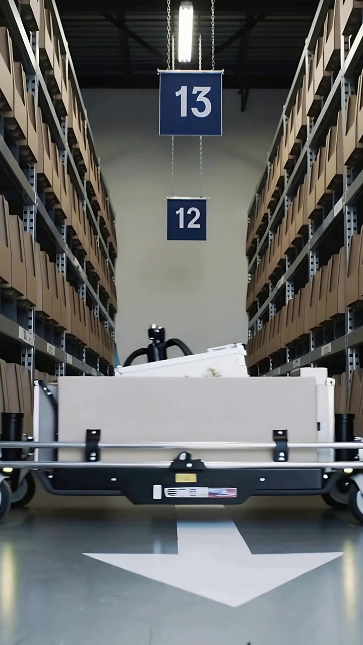 Vertical video: Entering from left, robot cart crossing aisle moving box, passing racks and arrow