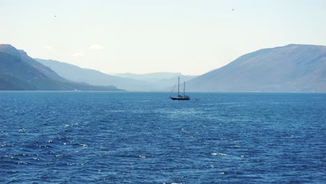 Sailing-yacht-sailing-on-the-blue-waters-of-the-Ionian-Sea-near-Corfu-Island,-with-beautiful-high-mountains-in-the-background