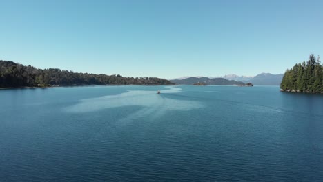 blue sky aerial follows sailboat motoring on deep blue patagonian lake