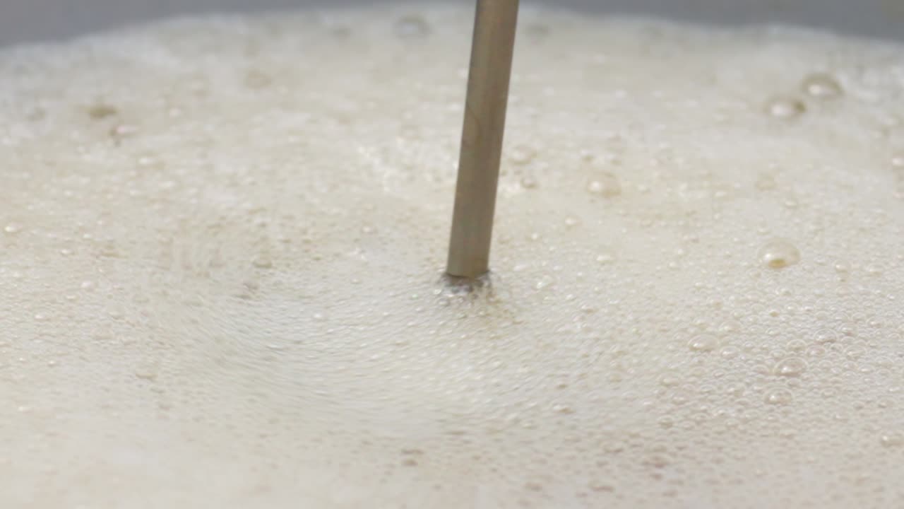 Macro Closeup at coffee mixing tool brewing foamy barista drink, stirrer in slow motion