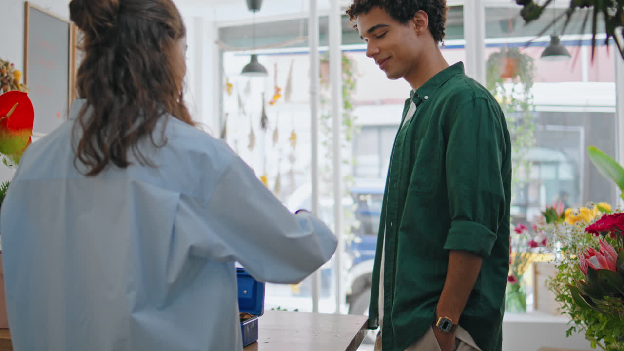 el cliente africano paga dinero en la caja de la floristería. el joven compra flores.