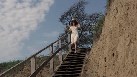 energetic woman hurrying downstairs sand beach holding straw hat on head.