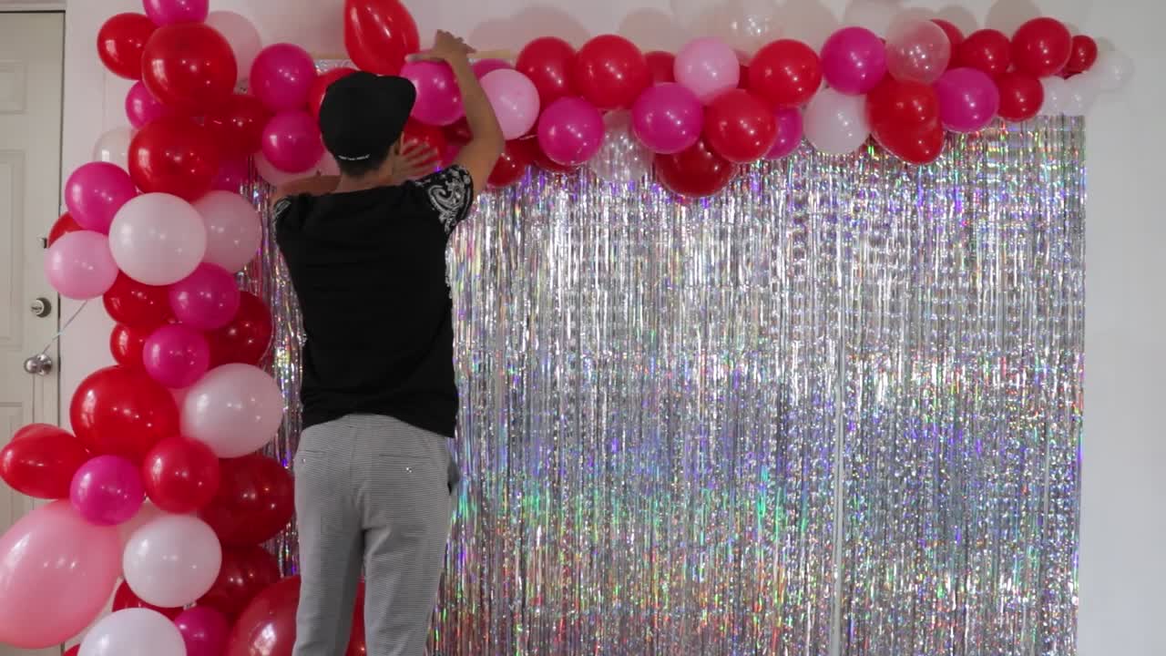 Young man decorating Valentine's day wall with fringes and balloons.