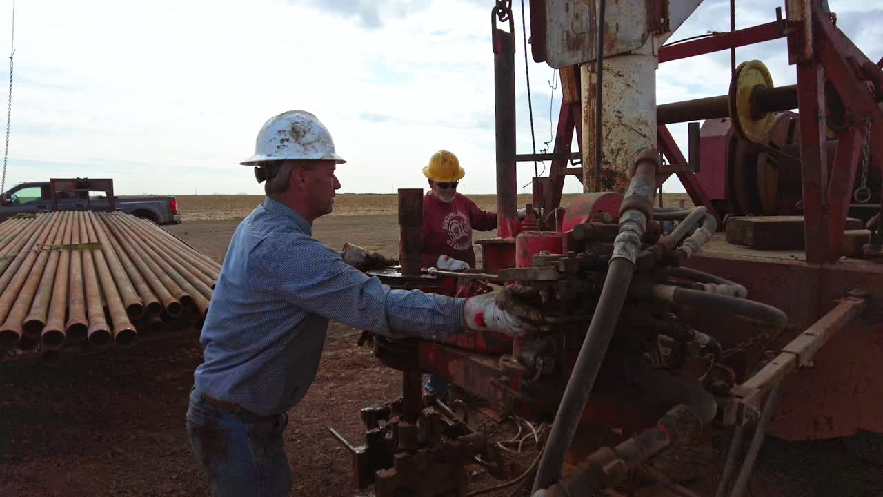 Hard-working men setting the equipment at the truck with drilling tower. Workers in protective helmets working in oil industry.