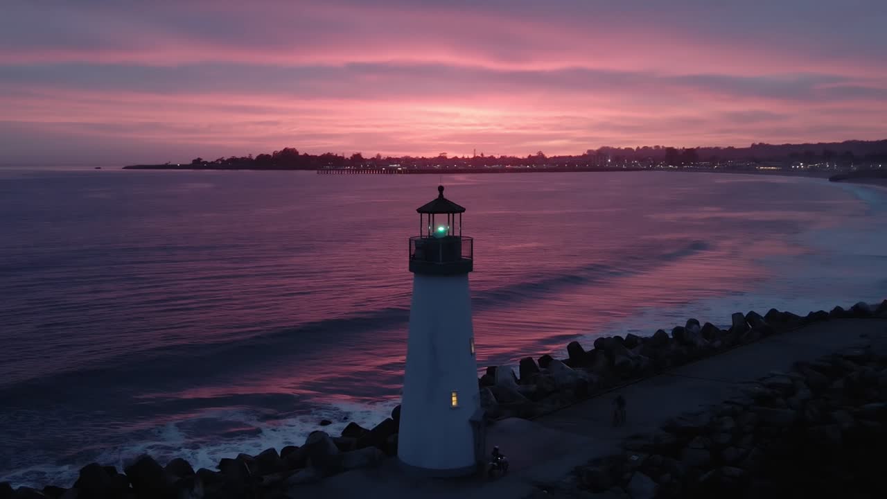 A dolly zoom drone shot pulling back revealing the Walton Lighthouse and the beachfront in Santa Cruz California in front of a stunning sunset with waves crashing in the Pacific Ocean