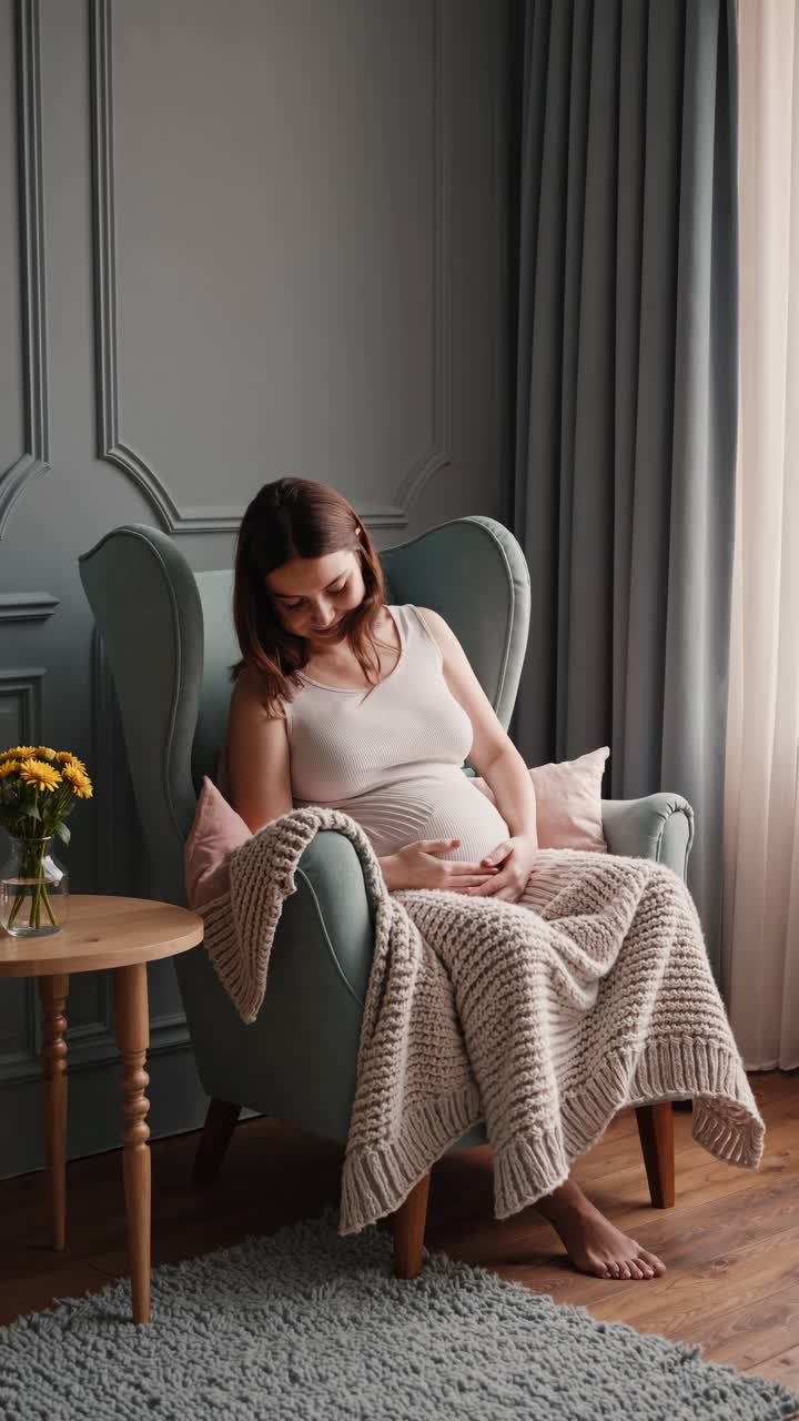 A serene video still of a pregnant woman sitting in an armchair, shot from a side angle