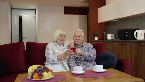 Abuelos-De-Una-Pareja-De-Ancianos-Hablando-Y-Usando-Una-Computadora-De-Teléfono-Móvil-En-Casa.-Compras-Por-Internet