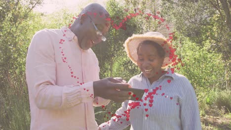 animation of hearts over senior african american couple using smartphone at christmas