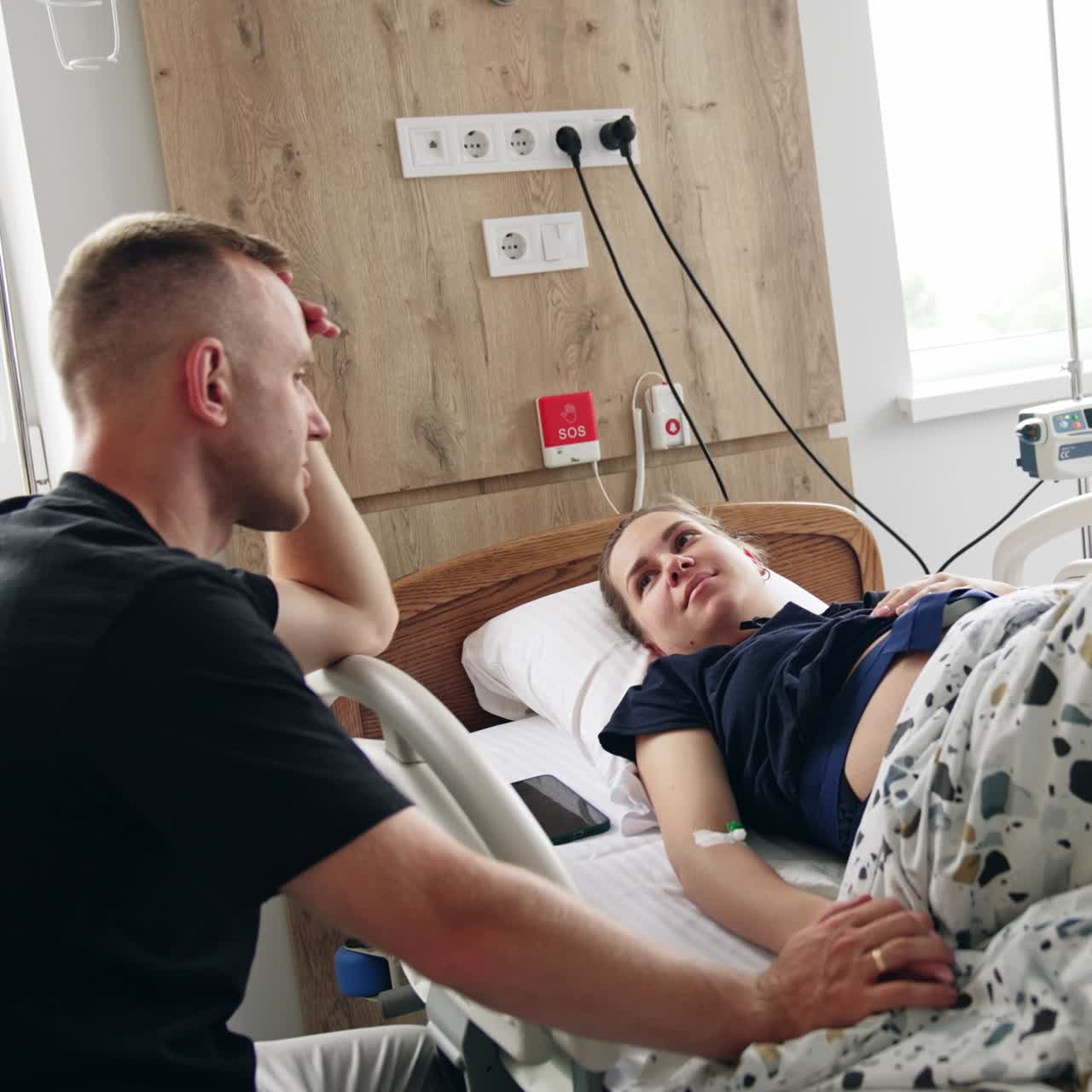 Man supporting his pregnant wife lying in hospital bed. Husband hold his wife's hand talking to her