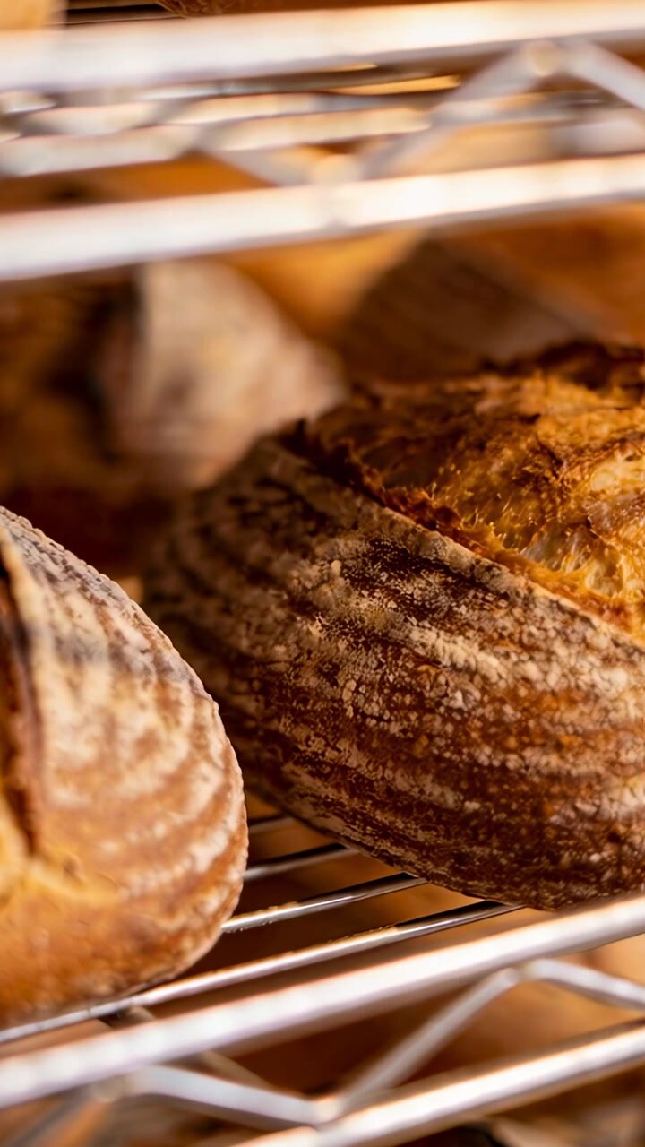 Vertical video: Shifting camera revealing scored sourdough loaf and 2nd loaf on rack, showing crust