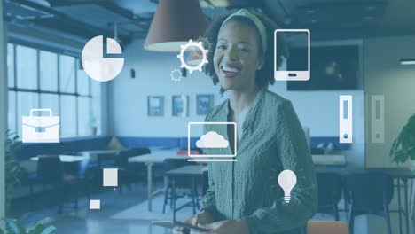 Animation of digital icons against african american woman using tablet and smiling at office
