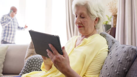 Happy-diverse-senior-couple-using-smartphone-and-tablet-in-sunny-living-room,-slow-motion