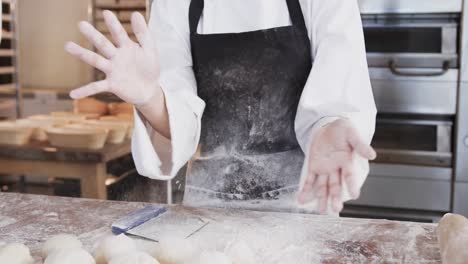 asian female baker working in bakery kitchen, brushing flour from hands in slow motion