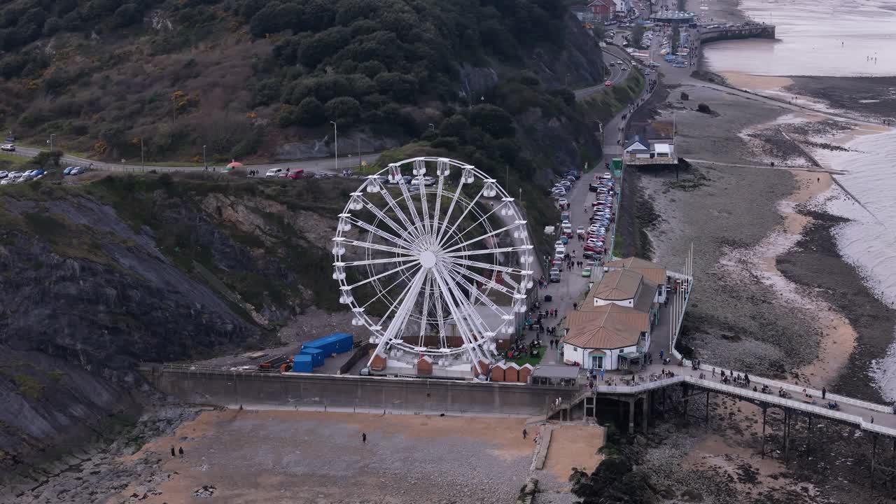A dynamic aerial telephoto orbit of the Ferris wheel at Mumbles Pier, near the coastline