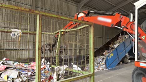 Tractor-with-claw-moves-paper-waste-from-bin-to-conveyor-at-recycling-facility