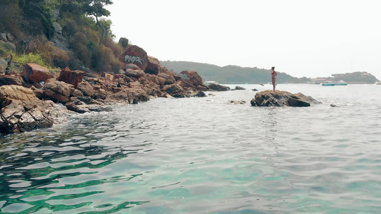 빨간 수영복 을 입은 긴 머리카락 을 가진  ⁇ 은 여인 이 돌 위 에 서 있다