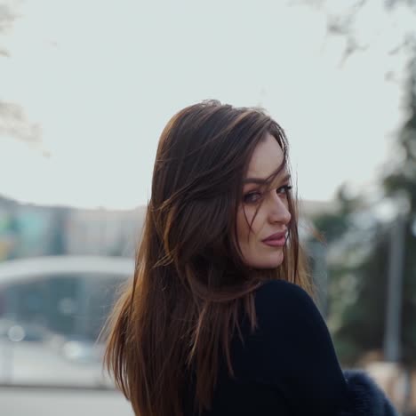 Portrait of charming young woman on the city park background. Beautiful model posing on camera outdoors. Motion camera around.