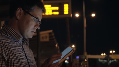 Young-man-writing-message-on-tablet-computer-while-waiting-on-stop-at-night-Thessaloniki-Greece