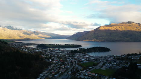 Setting-sun-casts-light-on-mountains-next-to-Queenstown,-aerial