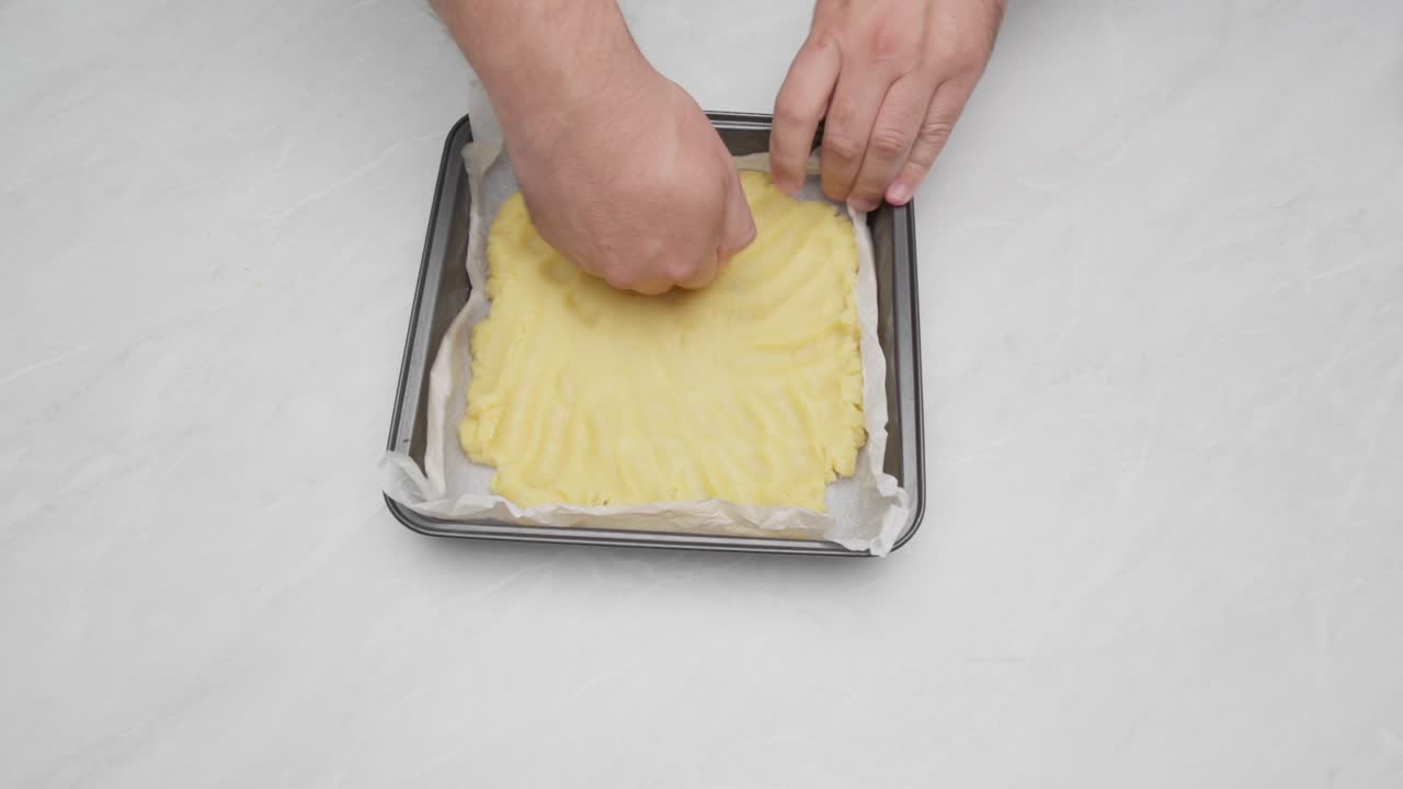 Mani che stendono uniformemente l'impasto della torta in una teglia foderata con carta forno