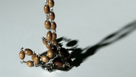 rosary beads casting a shadow and then falling on white surface