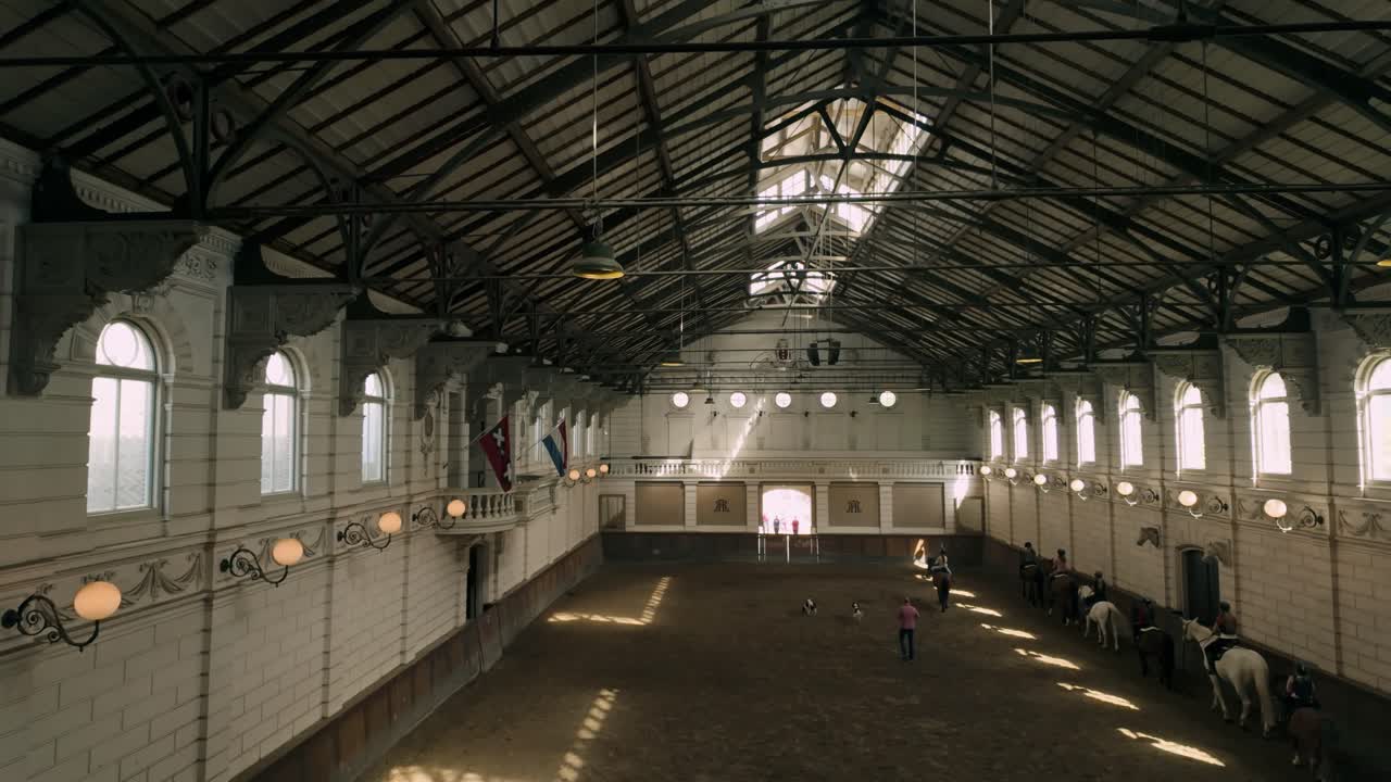 An aerial view of an indoor equestrian riding arena with riders and horses