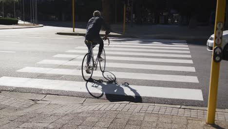 rear view of african american senior man riding bicycle crossing the road