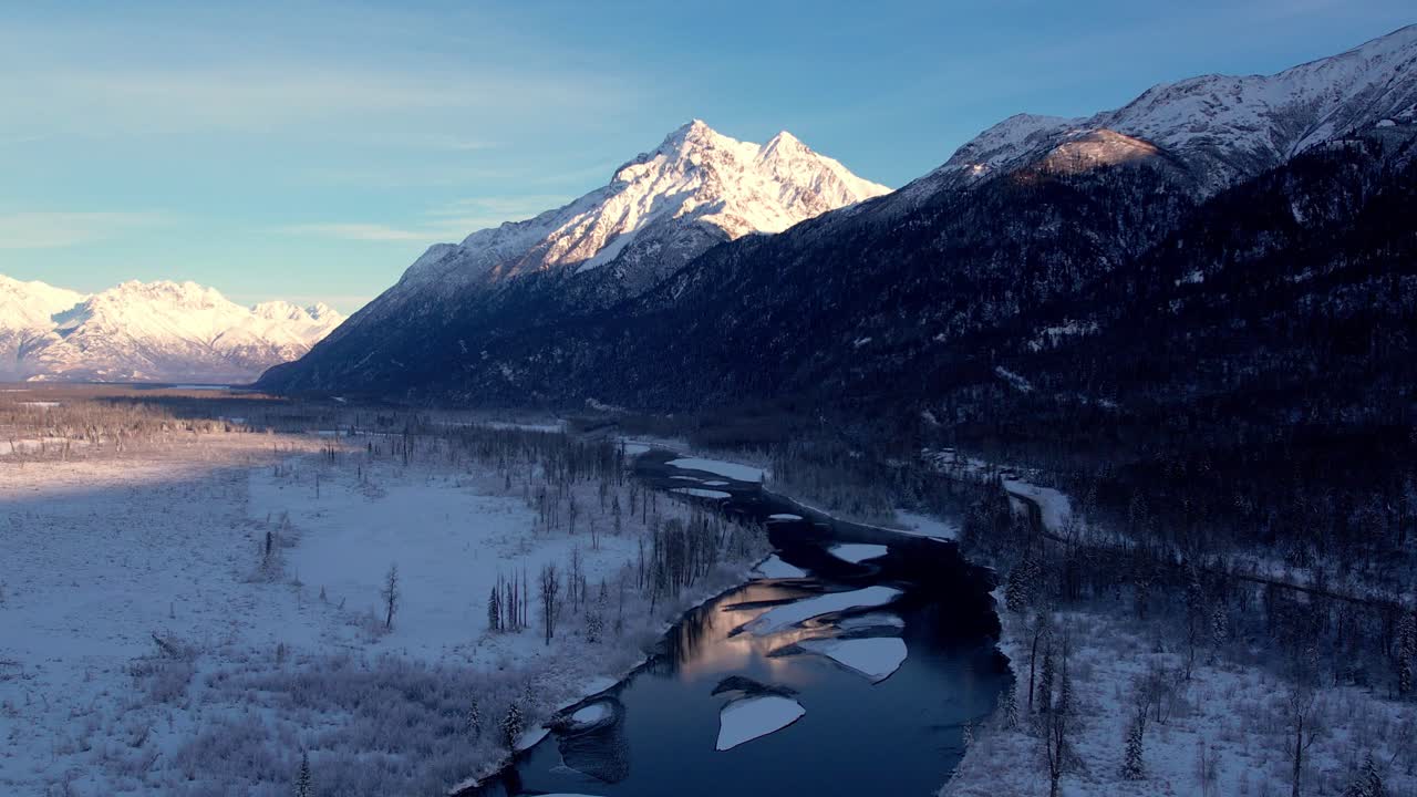 Drone lentää 70–80 jalan korkeudella varjon peittämän Knik-joen yllä. Jäätyneet jäälaikut muistuttavat kelluvia palapelin palasia. Lumihuippuinen Pioneer Peak näkyy auringonpaisteessa horisontissa. 4K, 60FPS.
