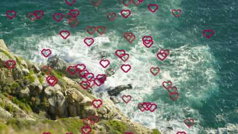 Red-heart-shapes-animation-over-ocean-waves-hitting-rocky-shore