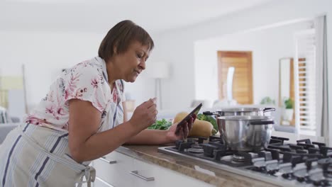 feliz mujer mayor afroamericana preparando comida en la cocina, usando una tableta y sonriendo