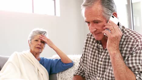 worried mature couple using smartphone on the couch