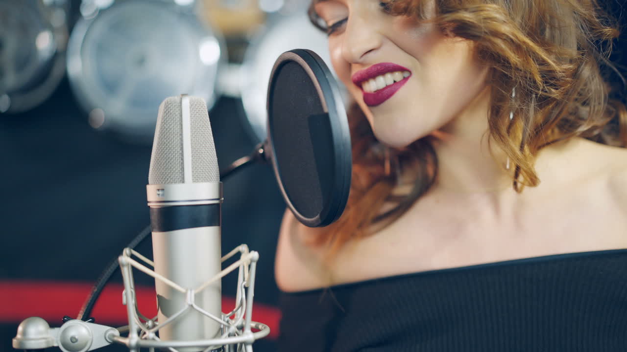 a talented woman with bright make-up is singing into a microphone in an audio recording studio. Singer is enjoying singing. Close-up