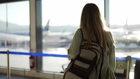 vista trasera de una turista que lleva una mochila caminando por la terminal del aeropuerto