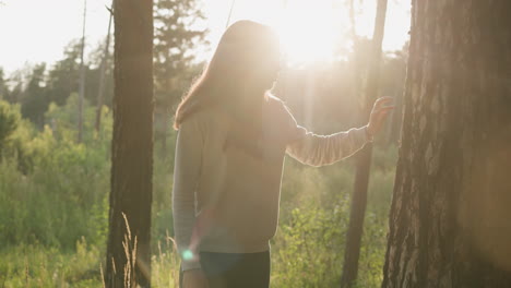 woman touches tree trunk on sunny day. love and respect for wildlife at sunset. lady with long loose hair feels empty and depressed walking in fresh air