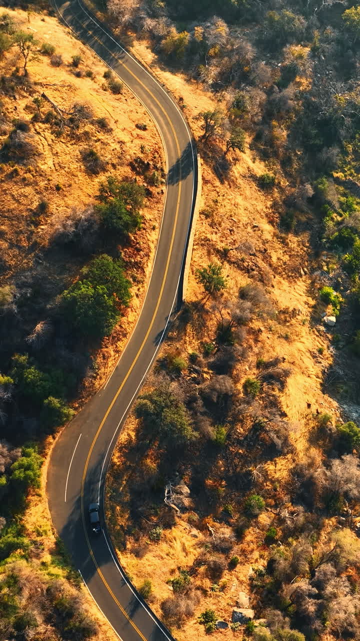 Car moving by the dangerous road on the mountain. Quick river with multiple rapids flowing at the foot. Top view. Vertical video